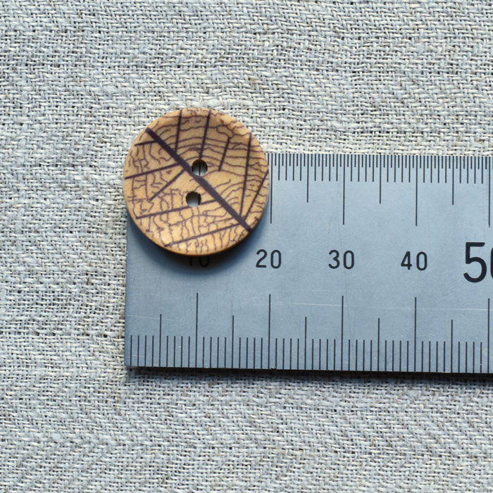 A single wooden button on a metal ruler to show the size