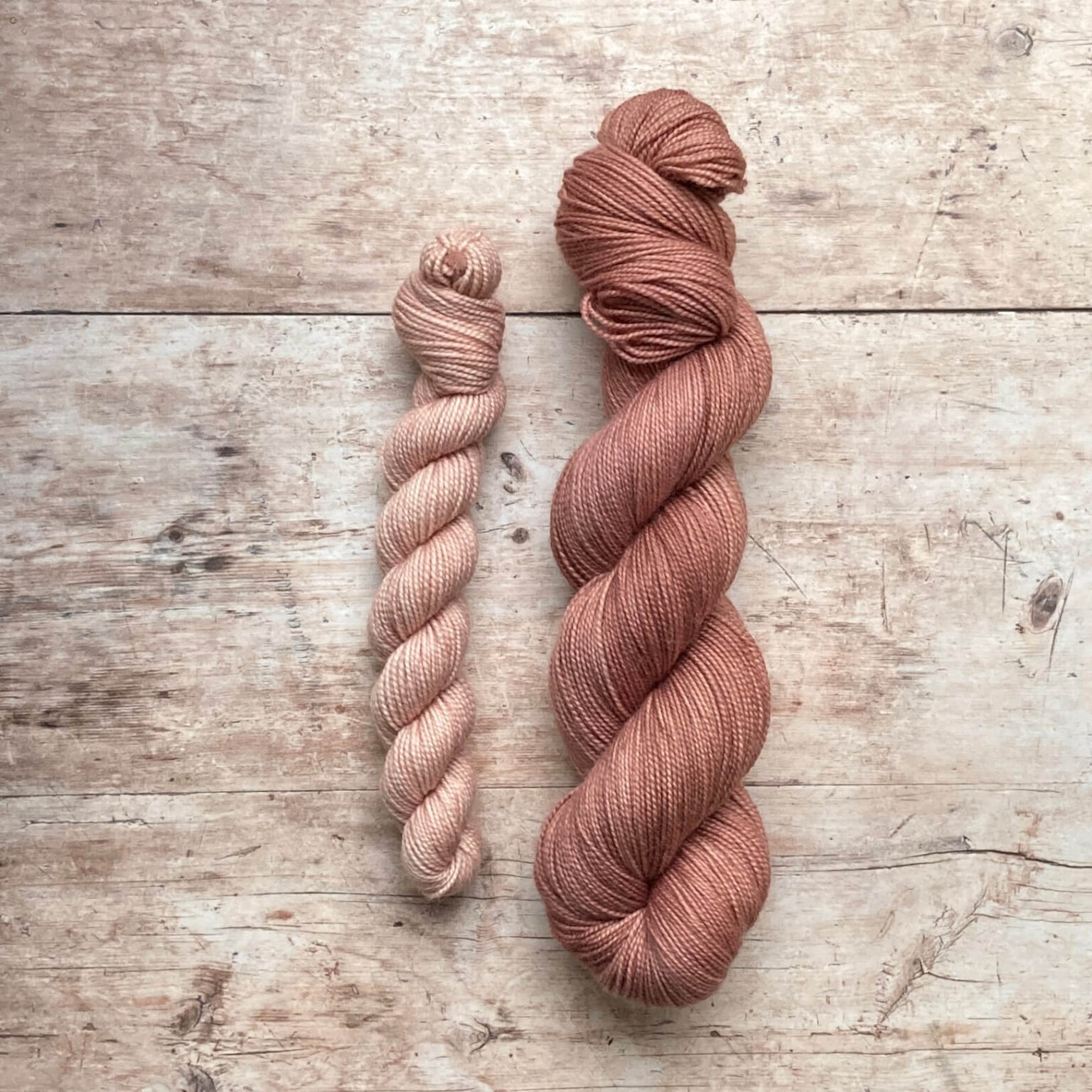A full skein of Classic Sock in a warm pink with a smaller skein in a lighter pink on a wood background
