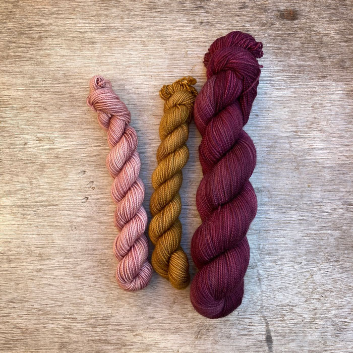 Two mini skeins in a soft gold and dusky pink with a full skein of deep burgundy