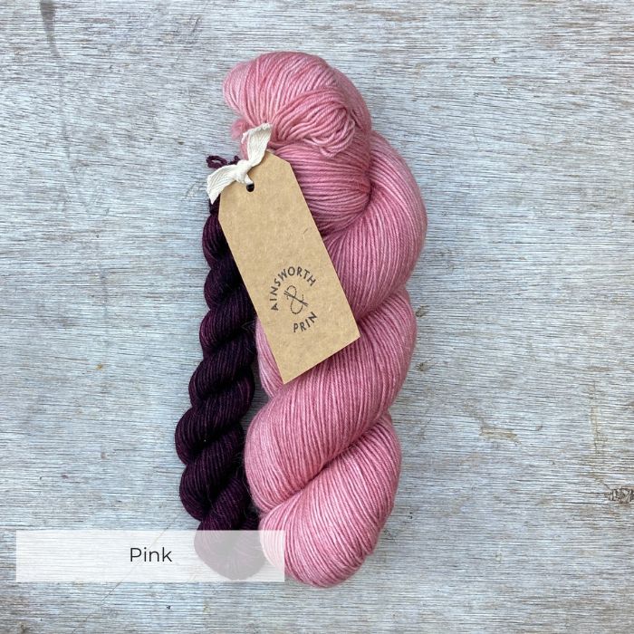 A full skein of pink sock yarn with a small skein of aubergine