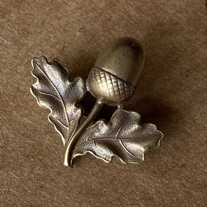 A pressed metal brooch in the shape an acorn with two oak leaves