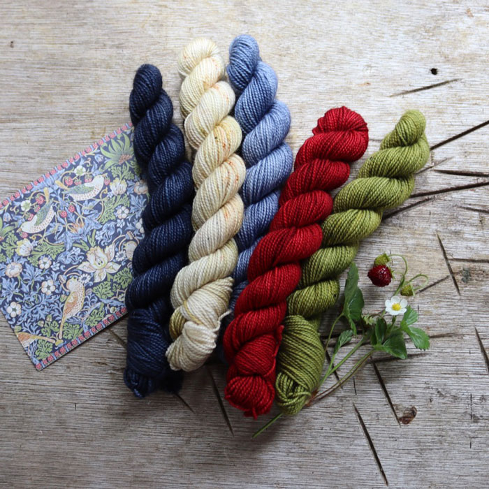 Five mini skeins laying on a wooden board with the card that inspired them and a sprig of strawberries
