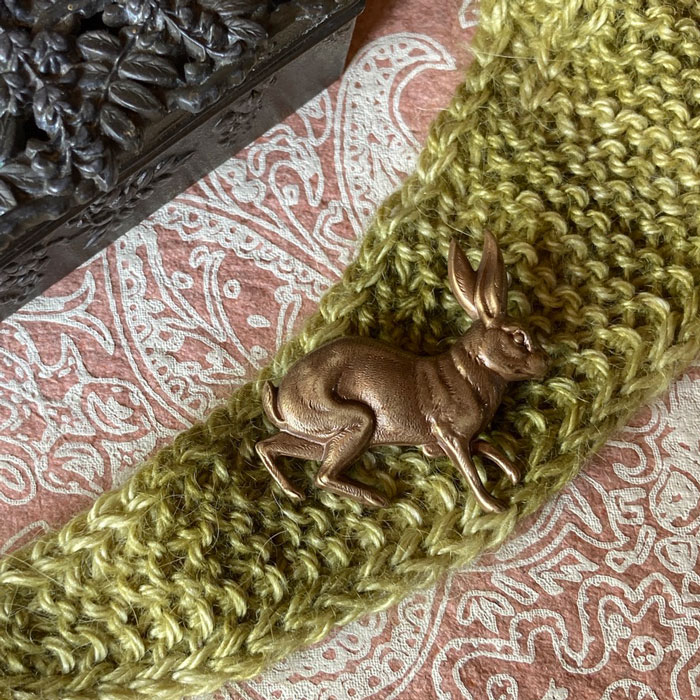 A close up of a hare shaped metal brooch laying on some knitting