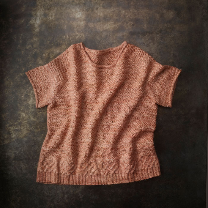 A short sleeve jumper with a knitted heart detail lays on a dark background