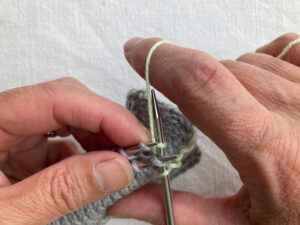 Hand taking yarn to back of back needle