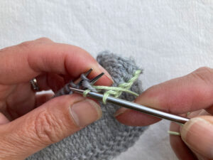 Spare needle pulling yarn through the front stitch on the front needle
