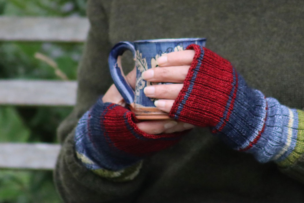 A woman's hands holding a mug and wearing a pair of red and blue colour block wrsit warmers