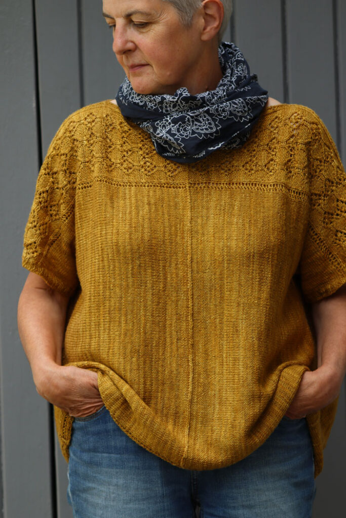Woman wearing a loose yellow jumper with navy blue and white scarf Hands in pockets of jeans