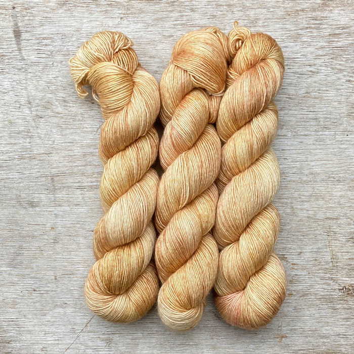 Three skeins of silky yarn in a soft buttercream yellow splashed with blush pink
