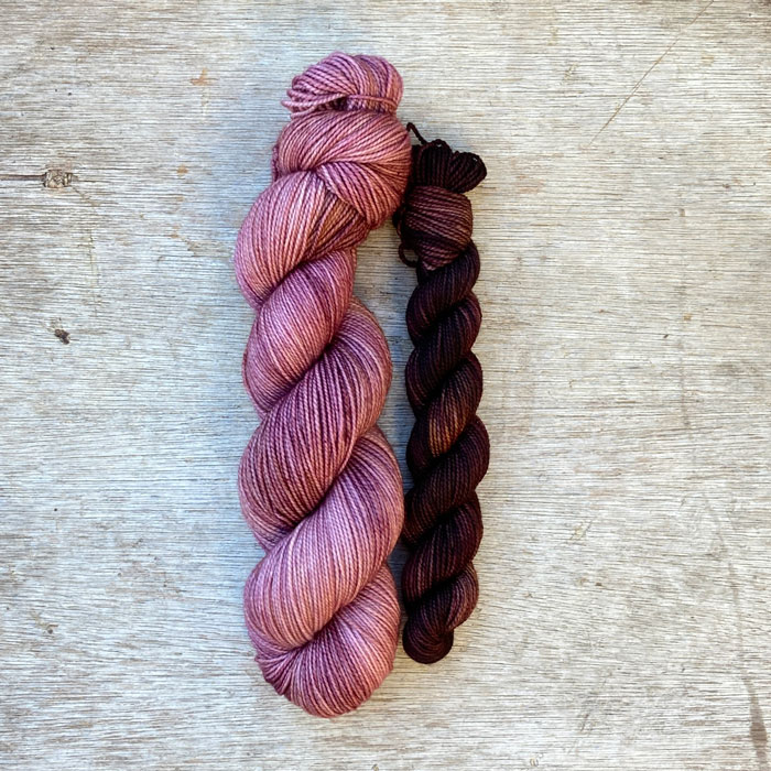 A full skein of merino sock yarn in shades of pink with splashes of gold and a smaller skein of dark maroon brown