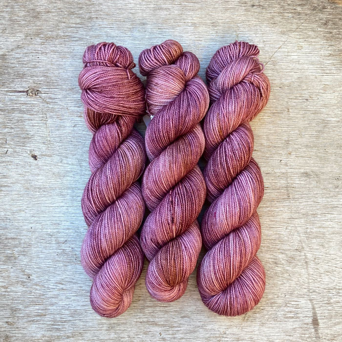 Three skeins of merino yarn in pinks and golds