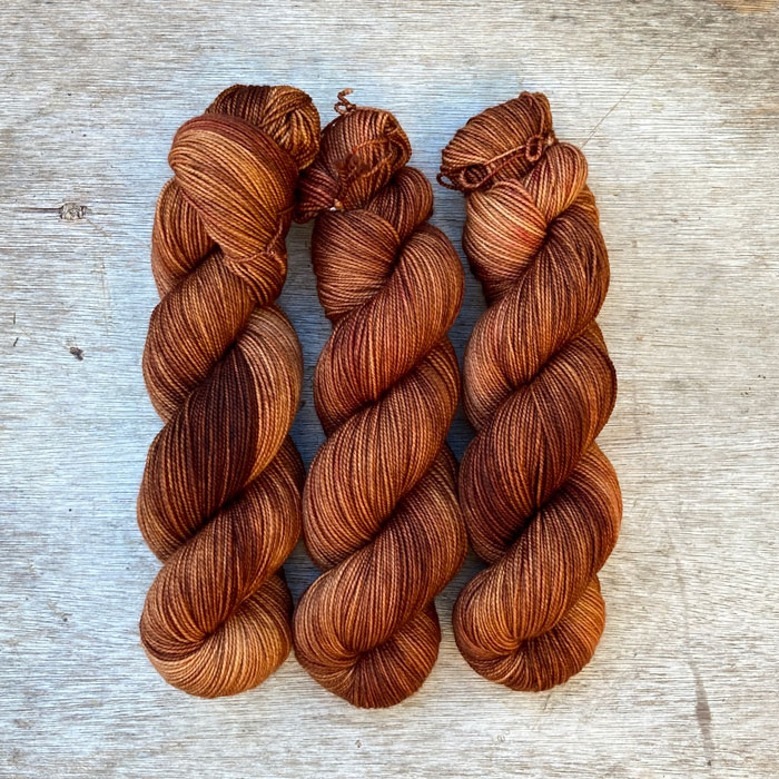 Three skeins of toffee coloured yarn with splashes of rose