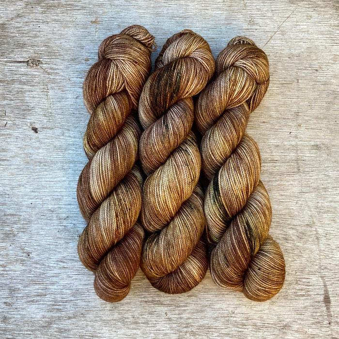 Three skeins of merino wool in cream splashed with brown and gold with green speckles