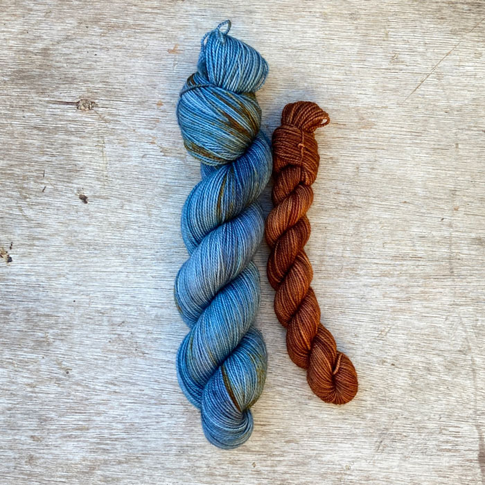 A full skein of merino sock yarn in shades of blue with splashes of gold and a smaller skein of toffee colour