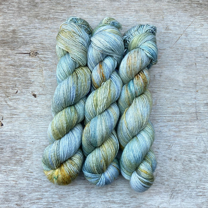 Three skeins of sock yarn in shades of blue, light grey and gold