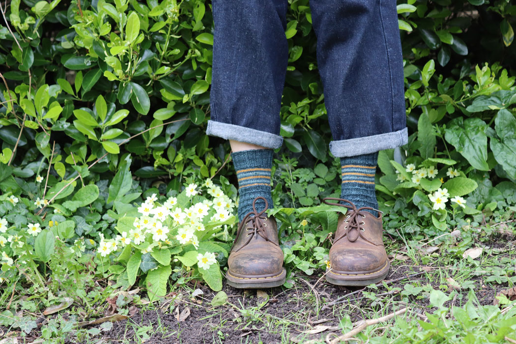 A pair of women' legs in front of a hedge. The legs of the jeans are slightly pulled up to show some striped socks