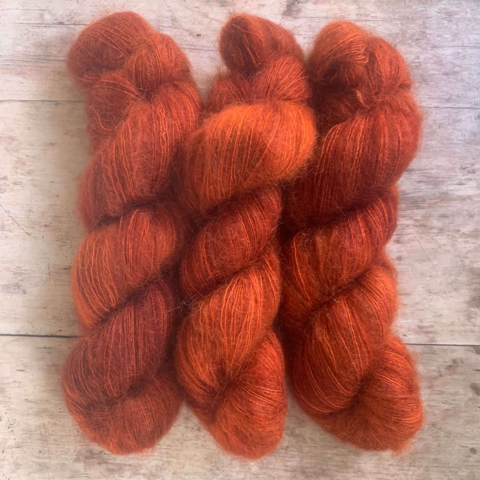 Three skeins of rusty orange mohair and silk lace yarn on pale wood background