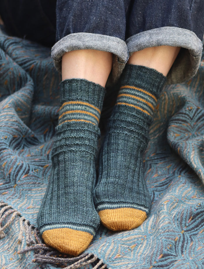 A pair of jean clad women's legs wearing striped blue socks on a blue woven blanket