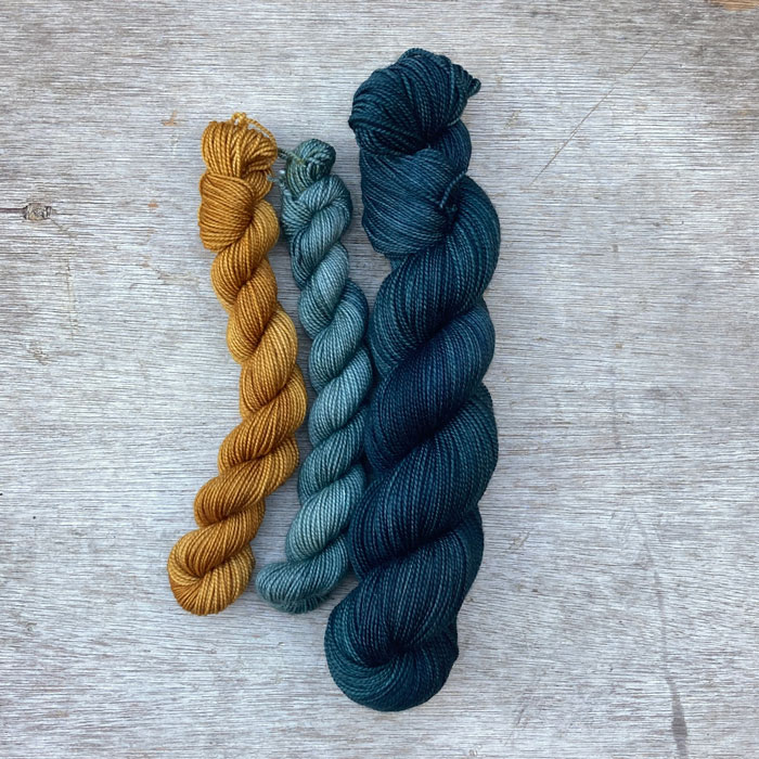 A full skein of dark blue teal yarn with two small minis one gold one mid blue