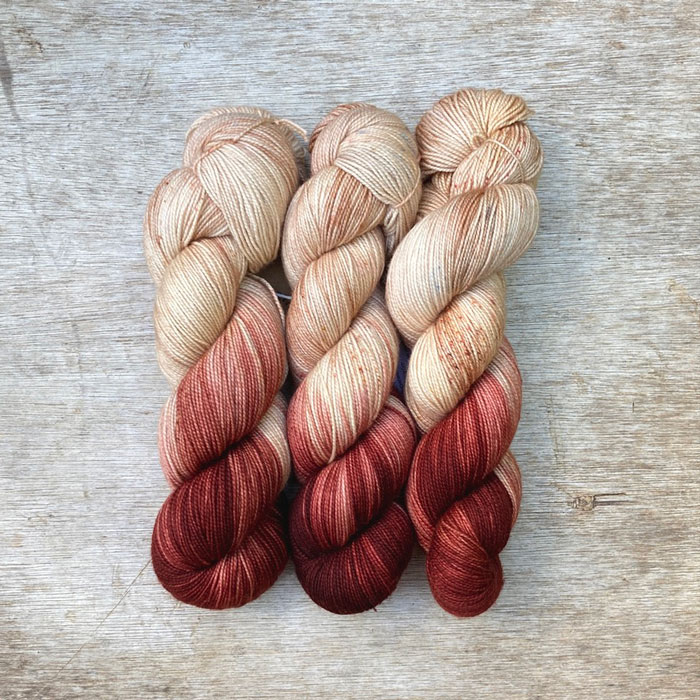 Three skeins of sock yarn in a pinky cream colour, lightly speckled and with one end of the skein dipped in a dark red