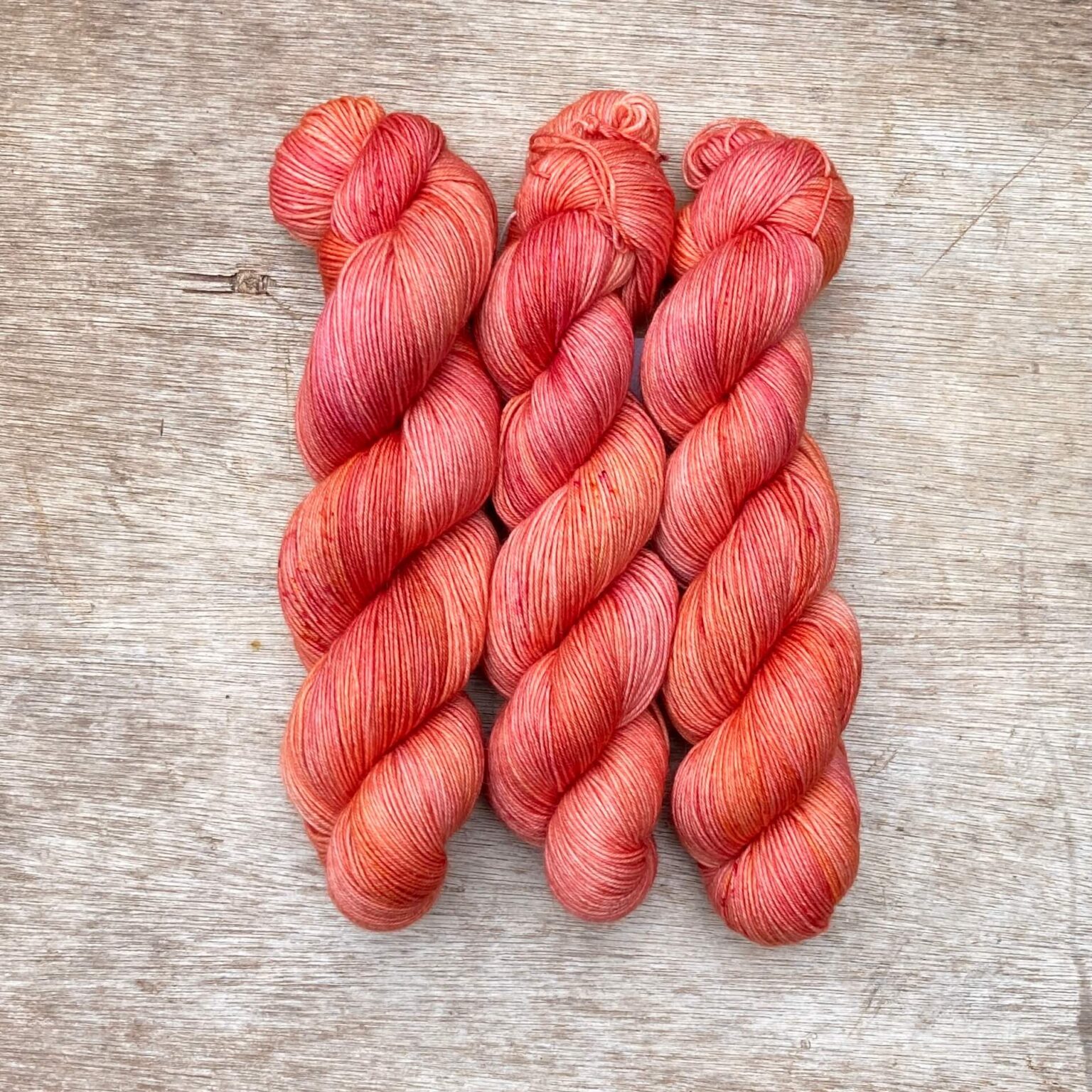Three skeins of merino mohair sock yarn in sunset shade of pinks and orange