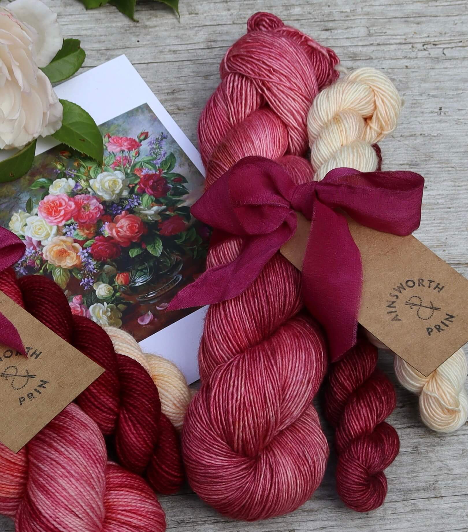 A single skein of rose pink Merino & Silk single with a mini skein in cream flushed oink and a deep crimson and burgundy