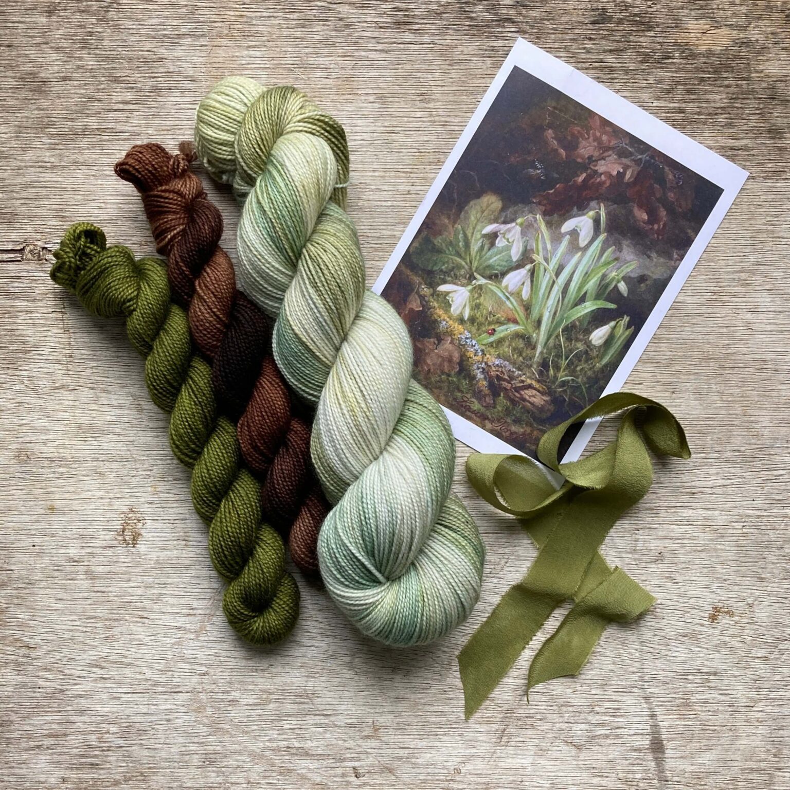 A full skein of pale green, grey and white sock yarn with two minis in moss green and brown and the picture that inspired them