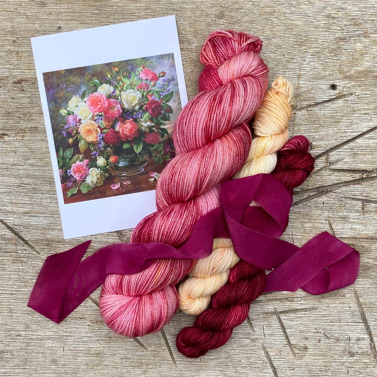 A single skein of rose pink Classic sock with a mini skein in cream flushed oink and a deep crimson and burgundy