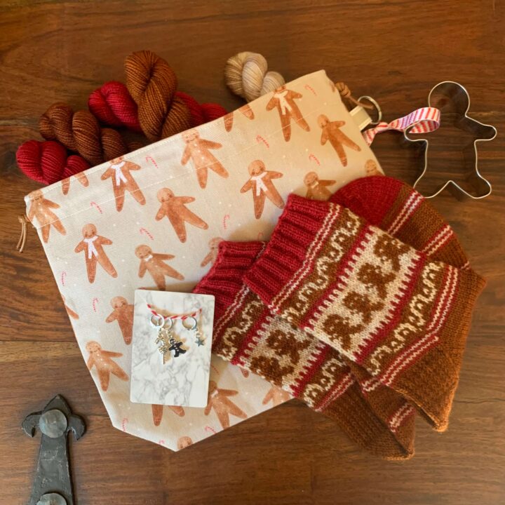 A folded pair of I'm a gingerbread man socks on a themed workbag with coordinating stitch markers a biscuit cutter and yarn