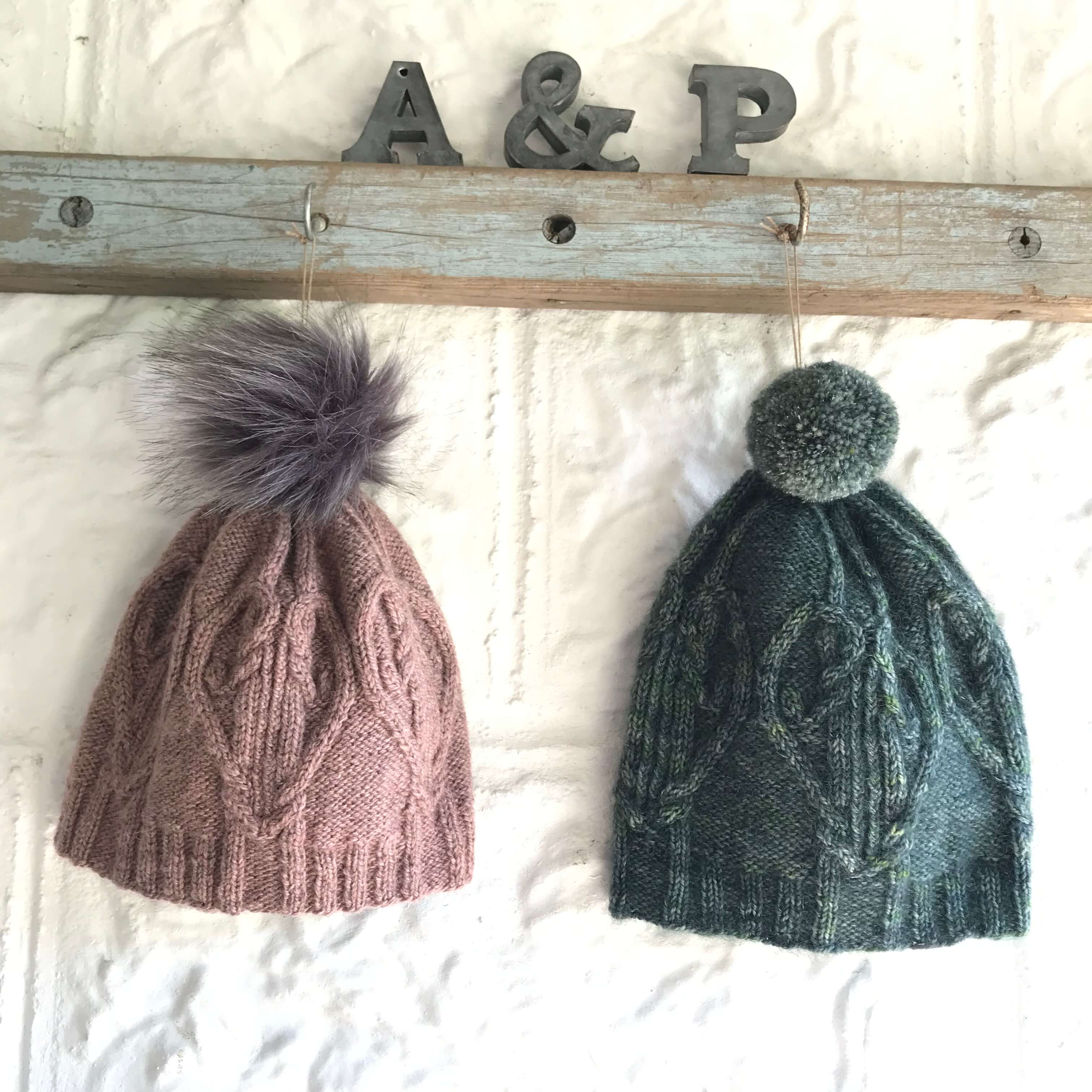 Two bobble hats with heart cable motif hanging on a rail