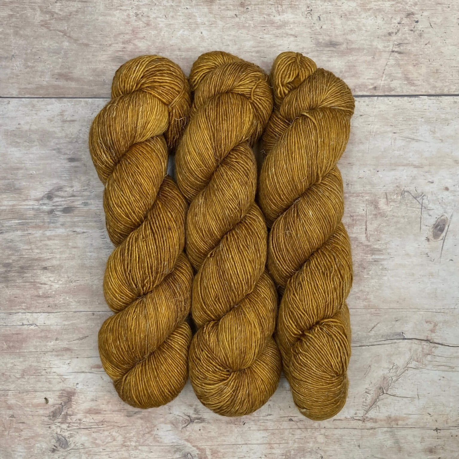 Three skeins of a wool and linen blended yarn in a golden mustard