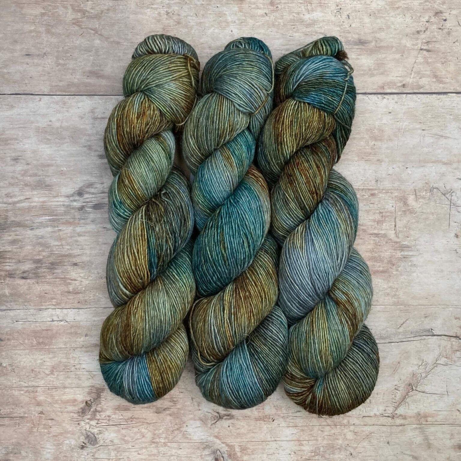 Three skeins of merino and linen in a mid blue green with splashes of golden brown