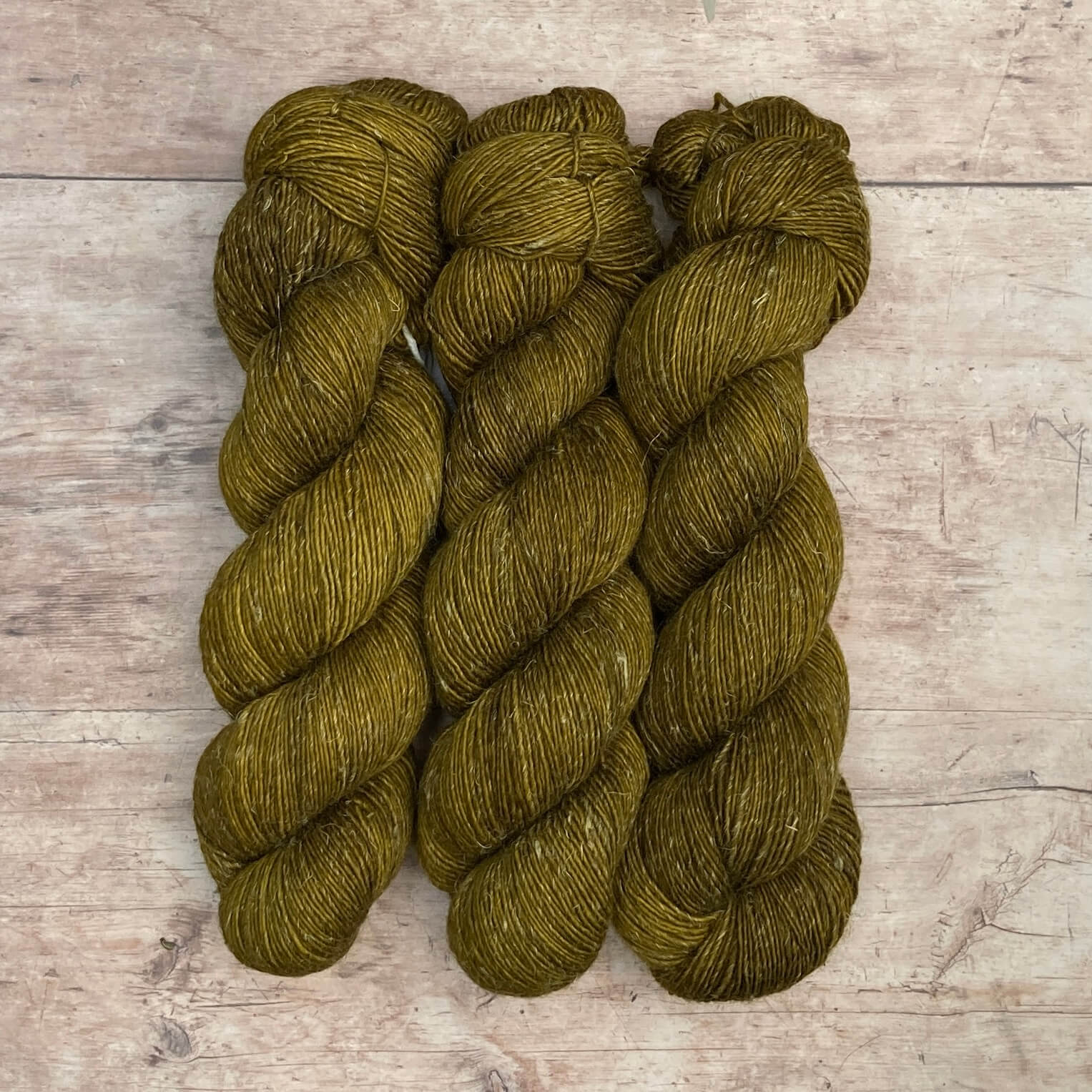 Three skeins of merino and linen in a mid blue green with splashes of golden brown