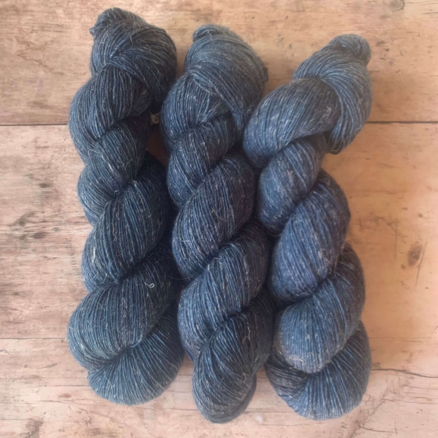 Three dark blue skeins of Merino yarn with linen on plae wood background