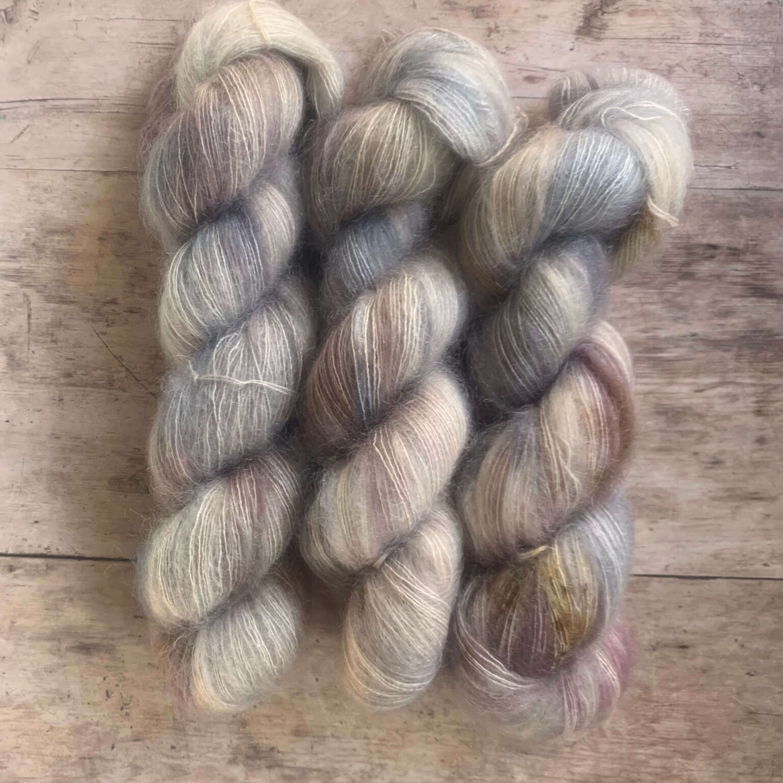 Three skeins Mohair Silk lace weight yarn in soft warm grey, speckled with brown on pale wood surface