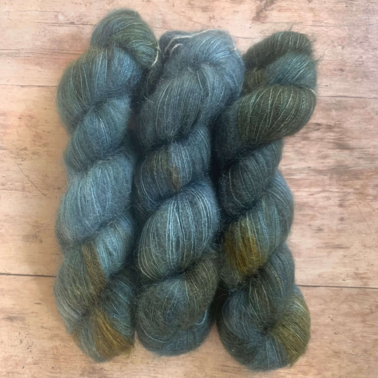 Three skeins of mid blue and rust variegated mohair and silk lace weight yarn on pale wood background