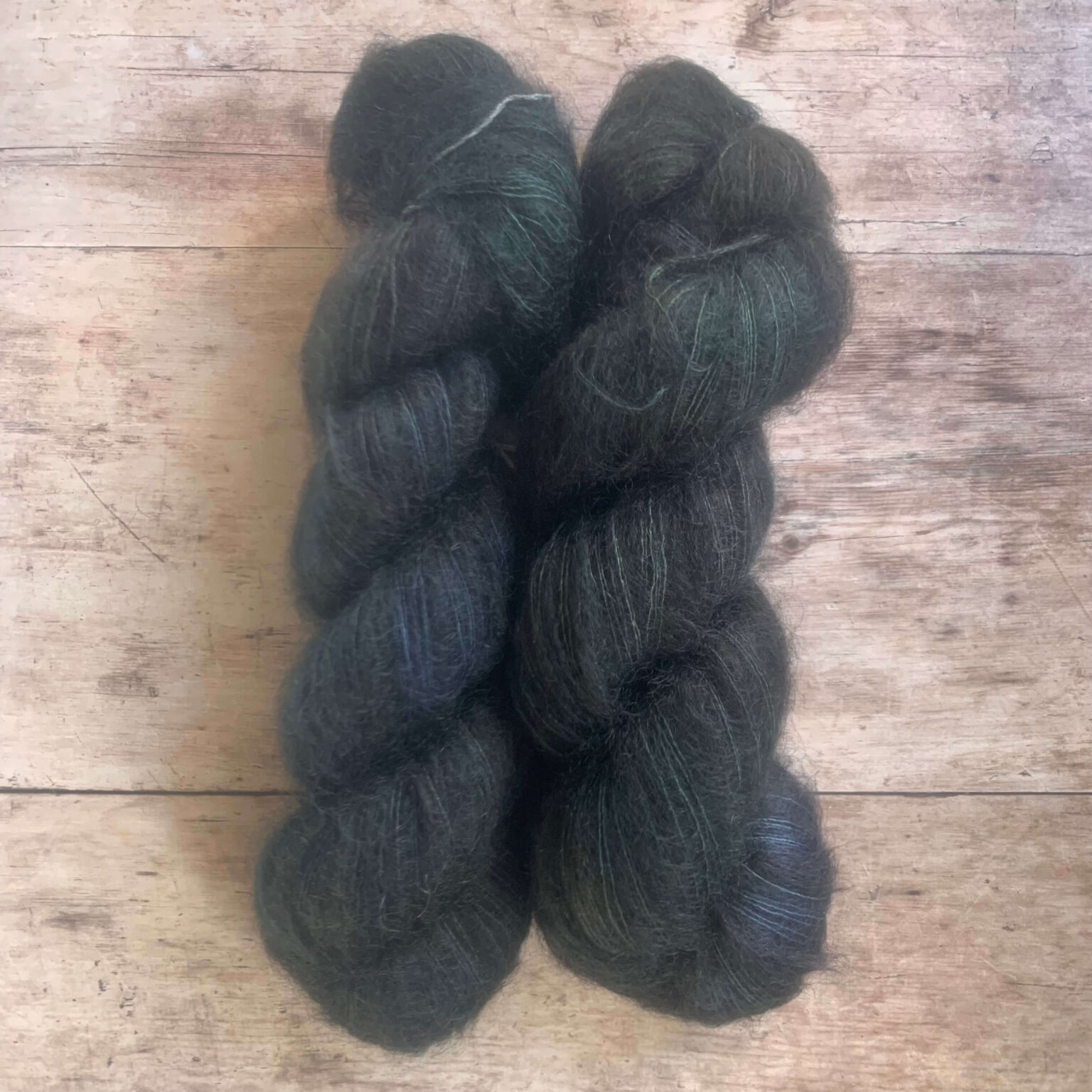 Two skeins of very dark blue variegated mohair and silk lace weight yarn on pale wood background