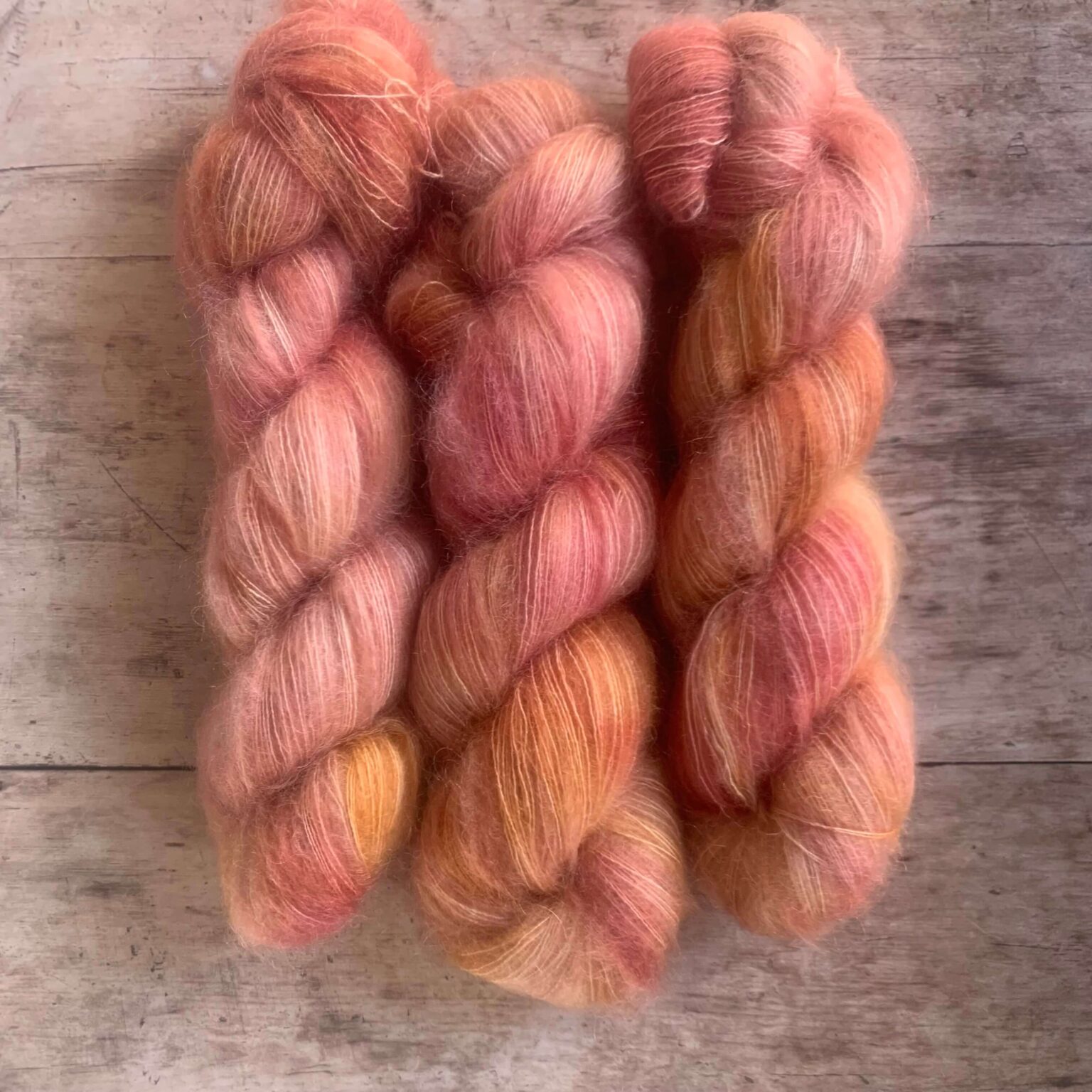 Three skeins of Pink and coral variegated mohair and silk lace yarn on pale wood background
