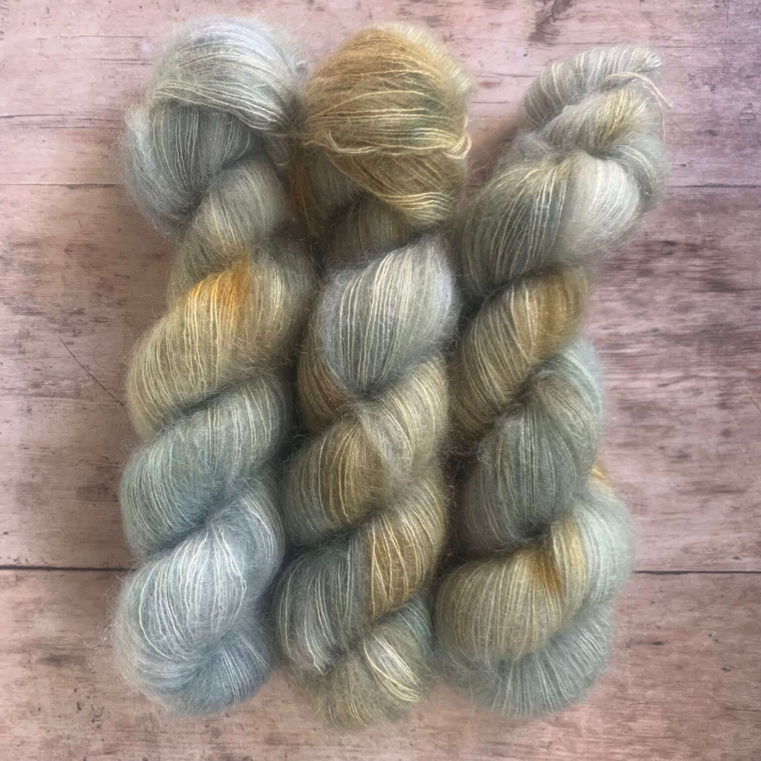 Three skeins of blue and rusty yellow mohair and silk lace yarn on pale wood background