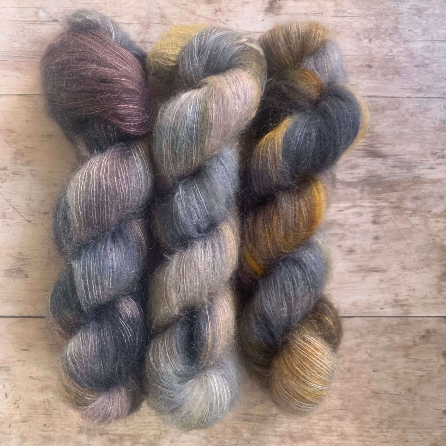 Three skeins of blue, yellow and orange mohair and silk lace yarn on pale wood background