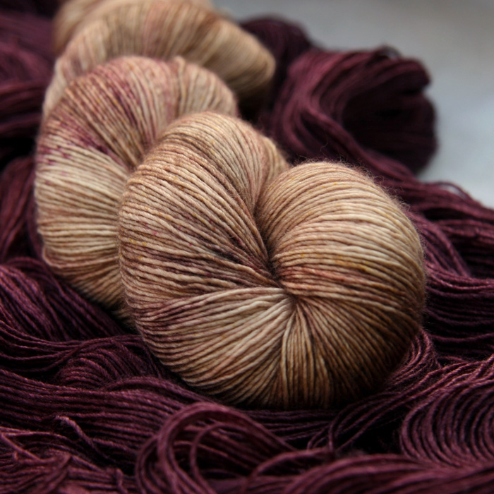 A skein of rich peachy pink yarn laying on an unwound skein of a rich red