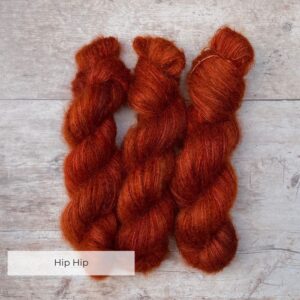 Three skeins of rusty orange mohair and silk lace yarn on pale wood background