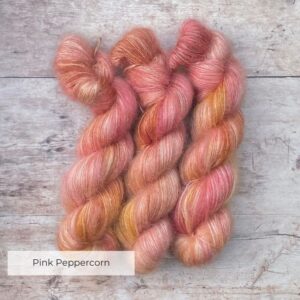 Three skeins of Pink and coral variegated mohair and silk lace yarn on pale wood background