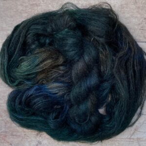 Two skeins of very dark blue variegated mohair and silk lace weight yarn on pale wood background