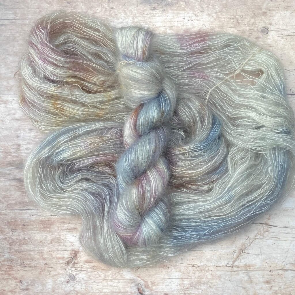 Two skeins Mohair Silk lace weight yarn in soft warm grey, speckled with brown on pale wood surface
