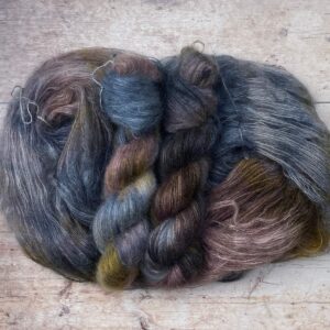 Three skeins of blue, yellow and orange mohair and silk lace yarn on pale wood background