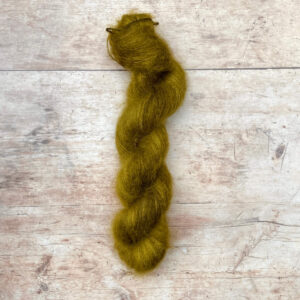 One skein yellow / green mohair silk yarn on pale wood background.