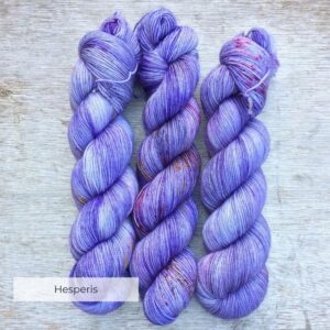 Three skeins of yarn dyed in shades of violet, grey and purple with splashes of pink and yellow