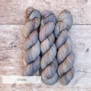 Three skeins classic sock in soft warm grey, speckled with brown on pale wood surface