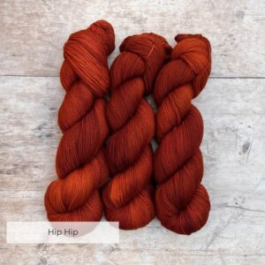 Three skeins of rusty orange Classic Sock yarn on pale wood background